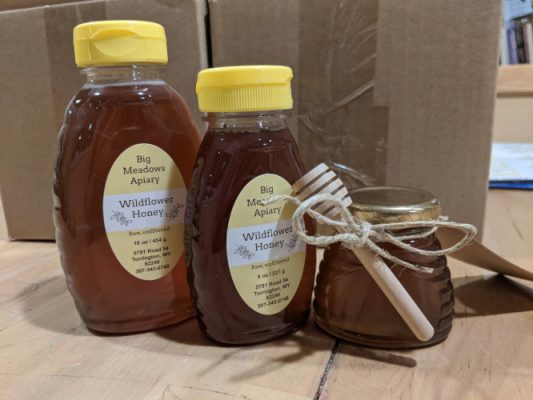 Bottles of Big Meadows Apiary honey with a wooden honey dipper
